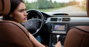 A confused looking woman sitting in the drivers seat of a car as it is driving down a road