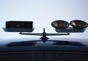 A scale with a speaker set on one side, and an amplifier on the other side, it is on top of a car and balanced in the middle