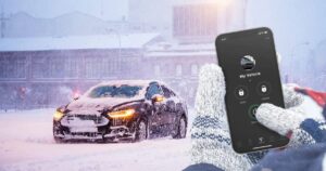 A person's hands pressing the start button for a remote start on their phone for their car which is covered in snow on a cold day