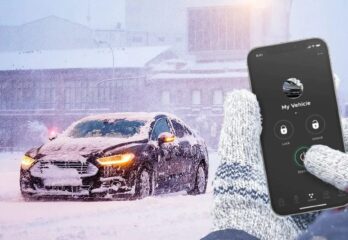 A person's hands pressing the start button for a remote start on their phone for their car which is covered in snow on a cold day