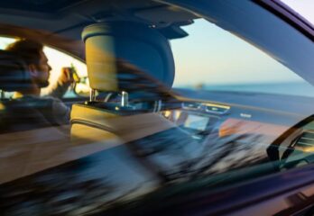 A view of a man driving a car on a road through the passenger side window