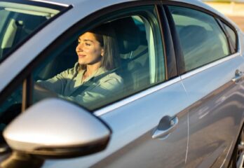 A woman driving a gray car with the sun on her face